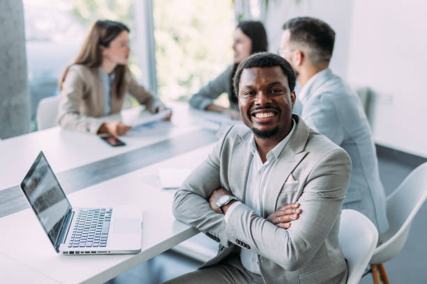 Portrait of handsome smiling businessman with his colleagues on meeting in board room. Young afro-american businessman using a laptop during a meeting in the office. Successful team leader and his team on a seminar in the office.